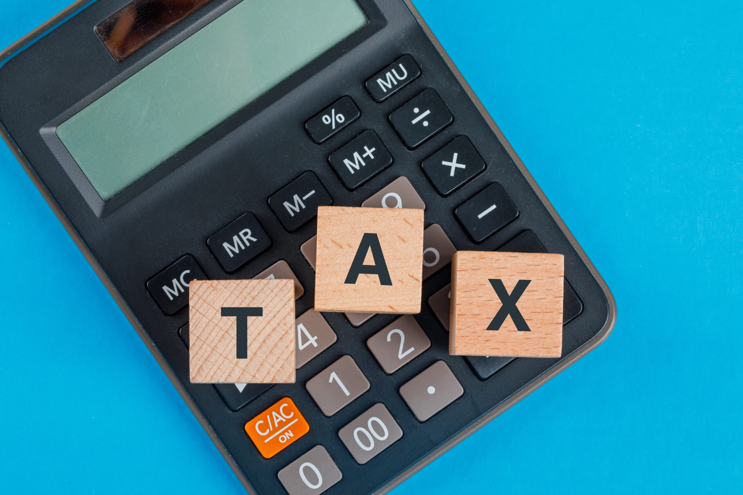 Tax planning concept with wooden cubes on calculator on blue background flat lay.